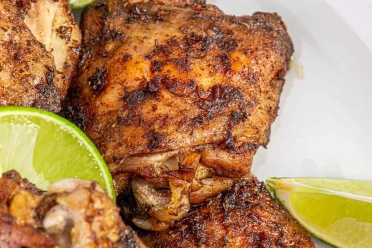 A platter of golden-brown oven-roasted jerk chicken with visible charred spices and fresh thyme garnish.