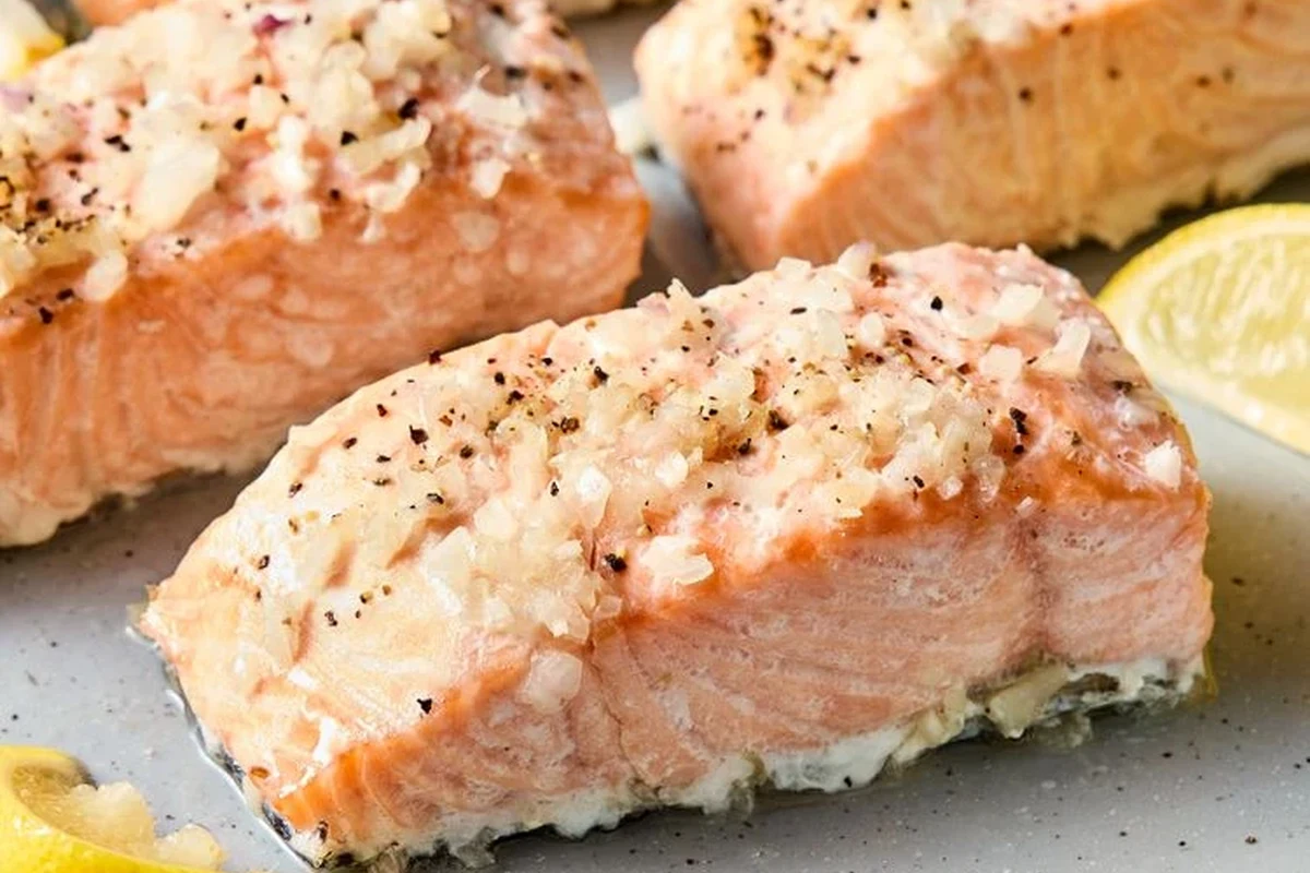A perfectly cooked, moist poached salmon fillet in a baking dish with lemon slices and fresh herbs.