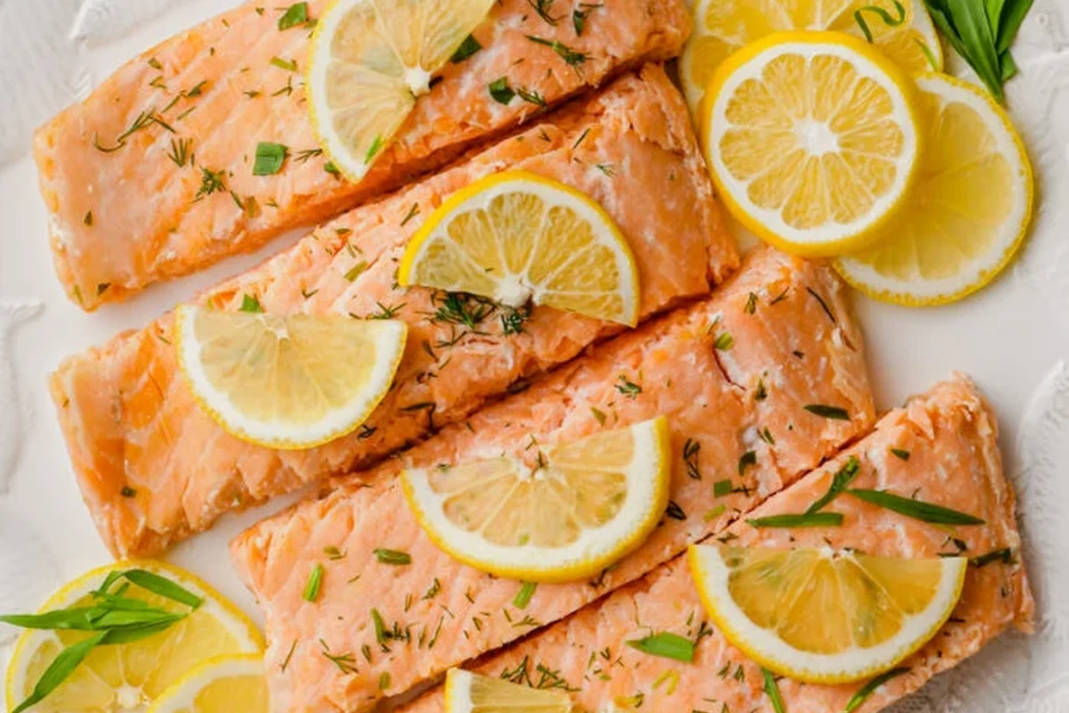 A perfectly cooked, moist poached salmon fillet in a baking dish with lemon slices and fresh herbs.