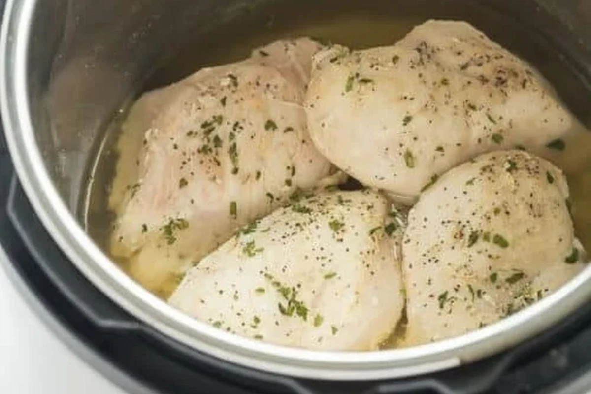 A stainless steel pressure cooker with cooked chicken breasts and aromatics inside.