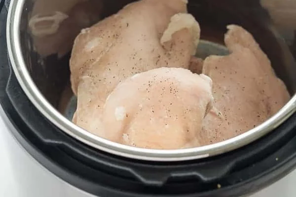 A pressure cooker filled with seasoned chicken breasts and broth, ready to be cooked.