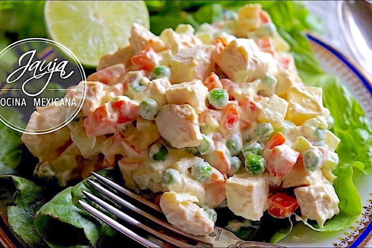 Ensalada de pollo con mayonesa servida en un tazón de cerámica, decorada con apio fresco y hierbas sobre una mesa de cocina.