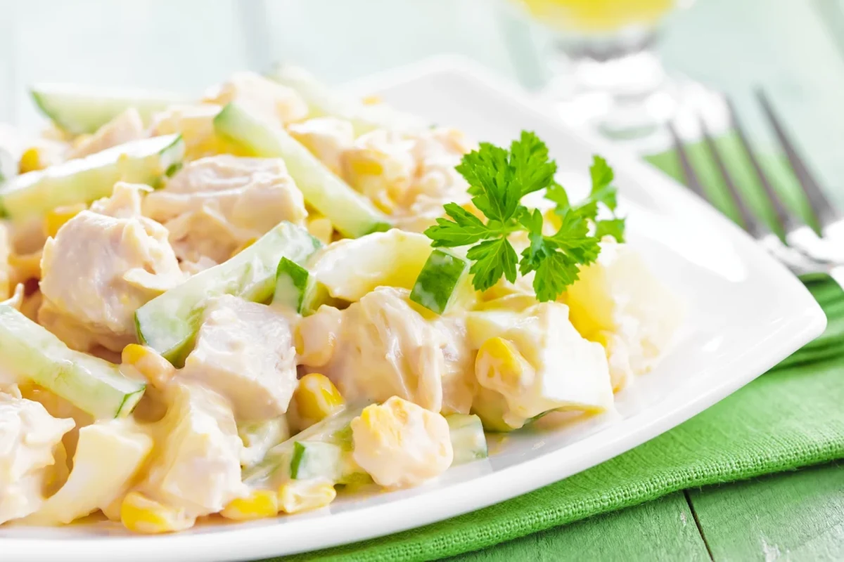 Ensalada de pollo con mayonesa servida en un tazón de cerámica, decorada con apio fresco y hierbas sobre una mesa de cocina.