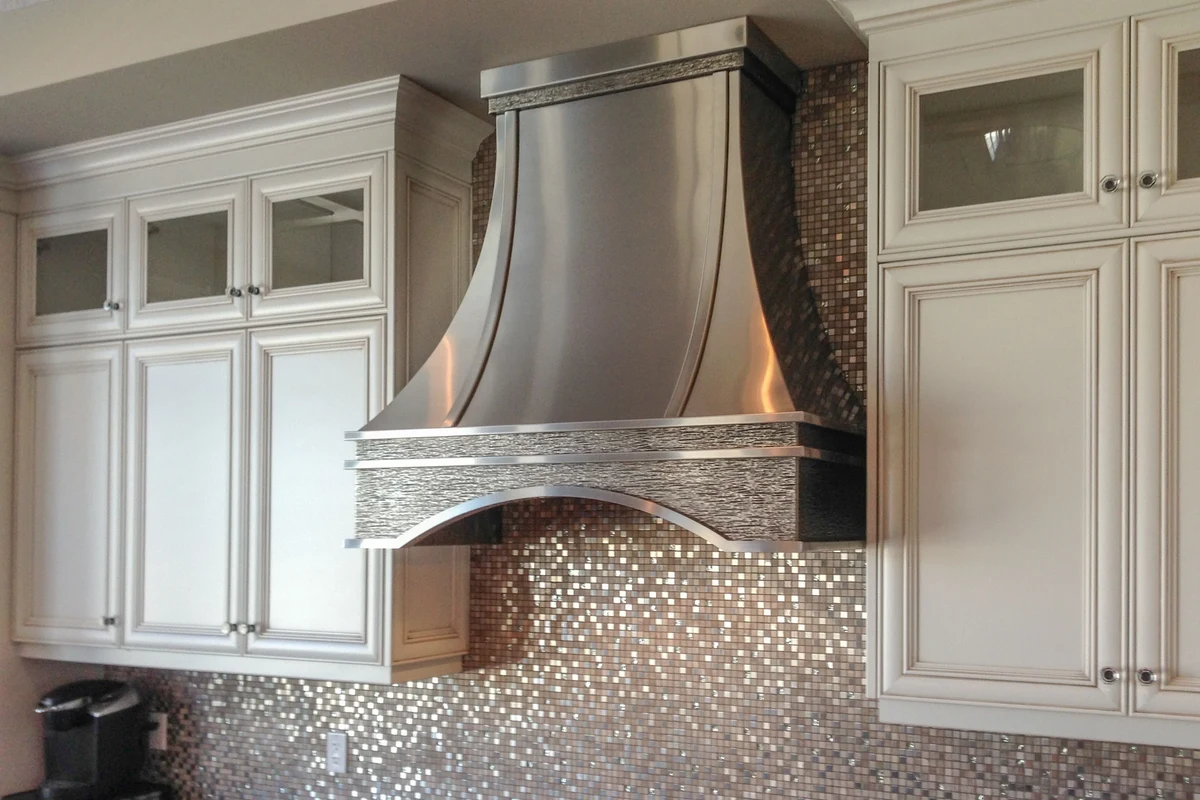 A modern, clean stainless steel range hood installed above a professional-style stove in a bright, contemporary kitchen.