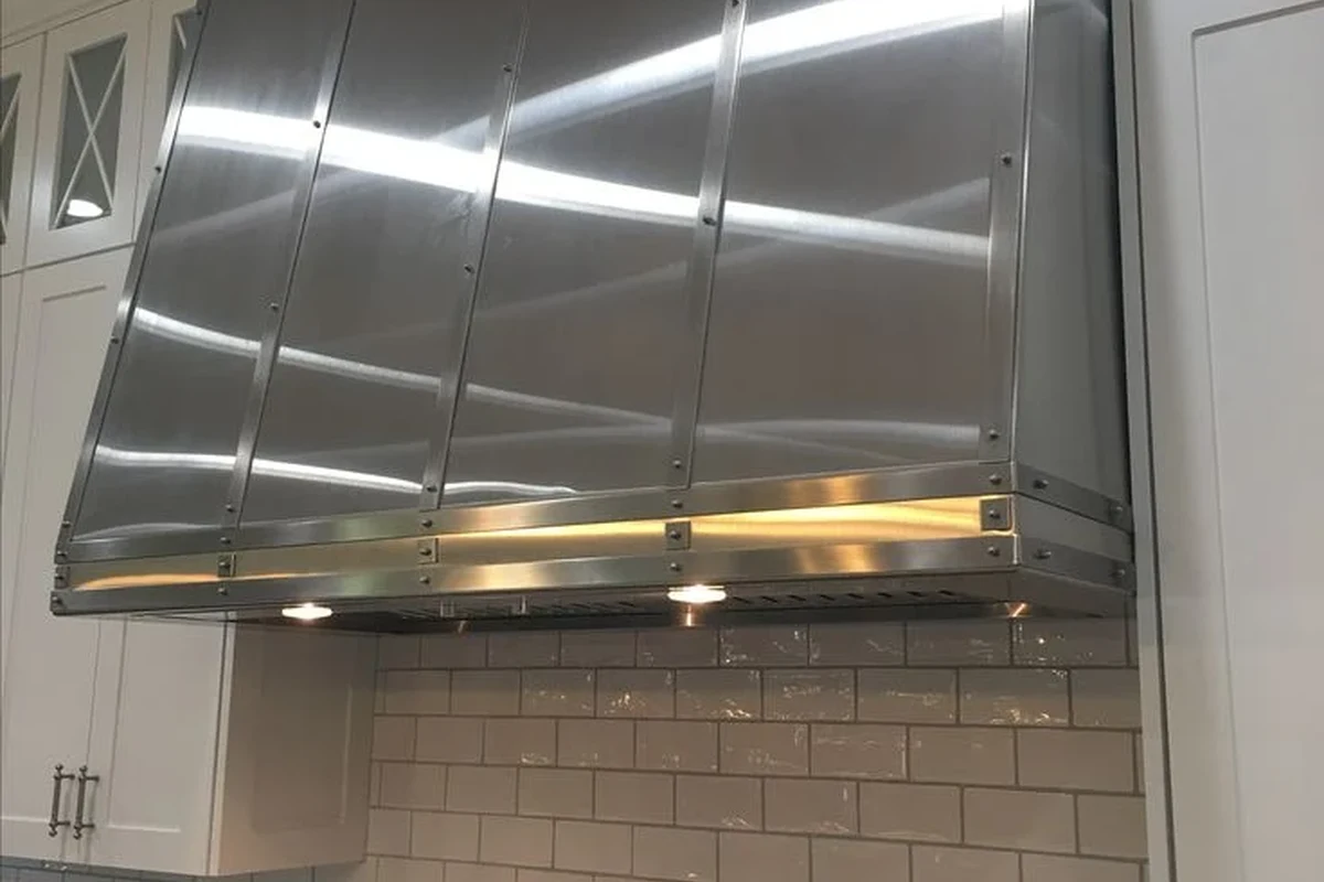 A modern, clean stainless steel range hood installed above a professional-style stove in a bright, contemporary kitchen.
