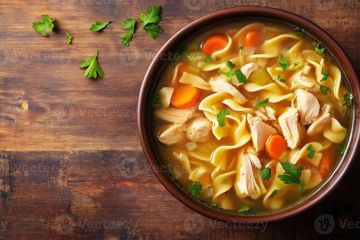 A steaming bowl of homemade chicken noodle soup featuring carrots, celery, and fresh herbs.