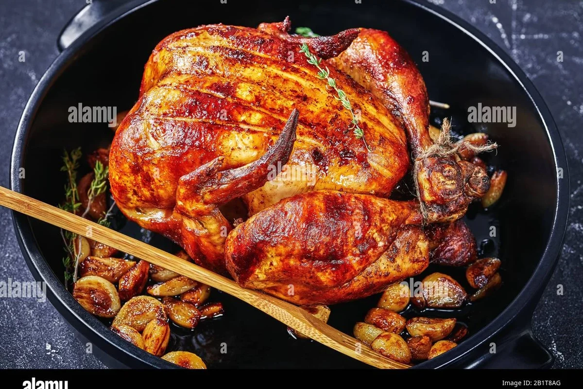 A perfectly golden-brown roasted whole chicken on a platter with fresh herbs.