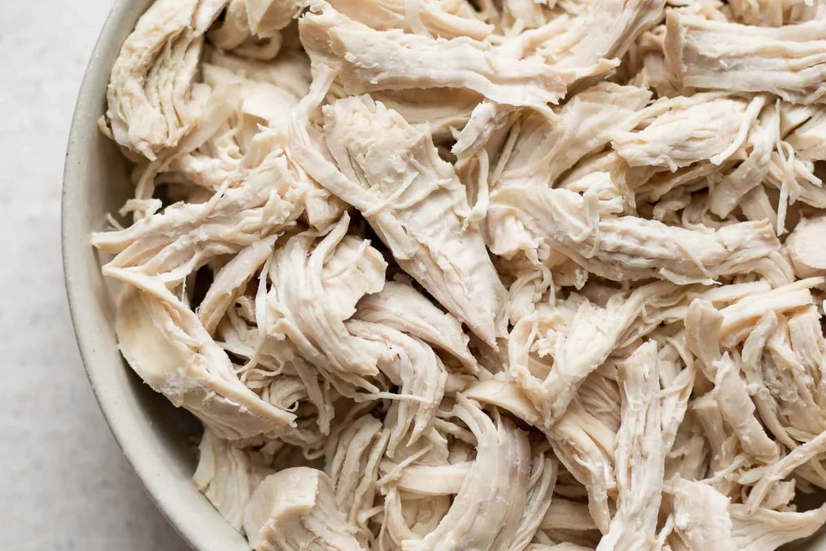 A bowl of perfectly shredded, juicy chicken thighs seasoned with traditional spices and fresh herbs.